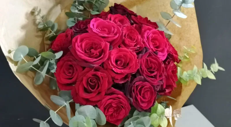 Dozen red roses with eucalyptus leaves wrapped in brown kraft paper