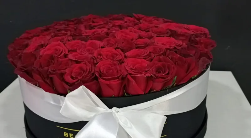 Round black box filled with red roses and white satin ribbon bow