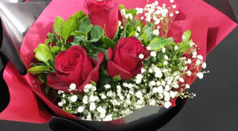 Three red roses with baby's breath in pink and black wrapper