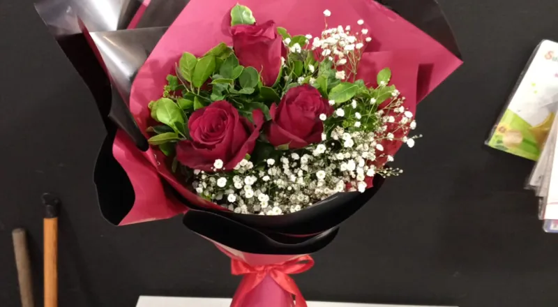 Three red roses with baby's breath in pink and black wrapper with ribbon