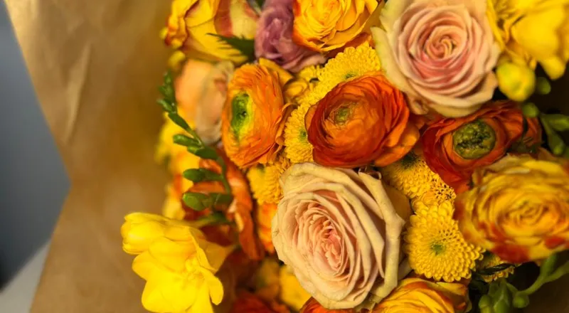 Yellow and orange ranunculus with freesia in brown kraft wrapper